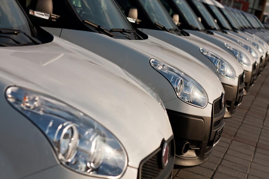 Flotte d'utilitaires commerciaux blancs alignés, vues de face. Détail des phares chromés et des pare-chocs noirs.