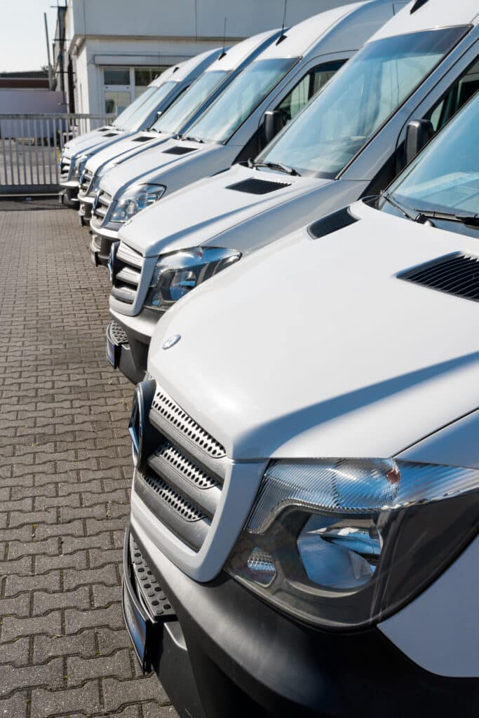 Flotte de fourgons utilitaires Mercedes Sprinter blancs neufs. Gros plan sur une rangée de fourgons utilitaires Mercedes-Benz Sprinter blancs garés. Flotte commerciale sous un soleil éclatant.